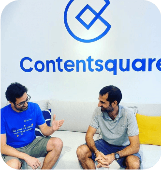 Two CS employees talking in the resting area of our offices with our CS logo on the wall